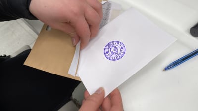Närbild på händer som sätter en röstningssedel i ett kuvert.
