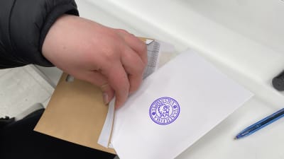 Närbild på händer som sätter en röstningssedel i ett kuvert.