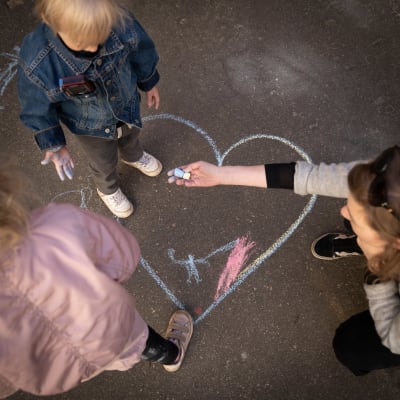 Äiti ja pienet lapset piirtävät katuliiduilla sydäntä asfalttiin.