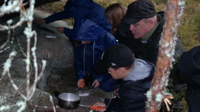Utomhuspedagogen Patrik Berghäll lär elever att göra upp eld under en stor sten