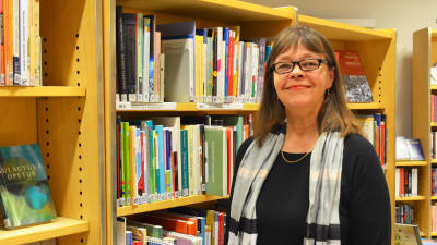 Bibliotekschefen Margareta Kull-Poutanen ser nöjd ut. Står framför bokhyllor.