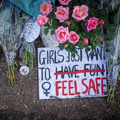Blommor på marken. Bredvid en skylt med texten "Girls just want to feel safe".