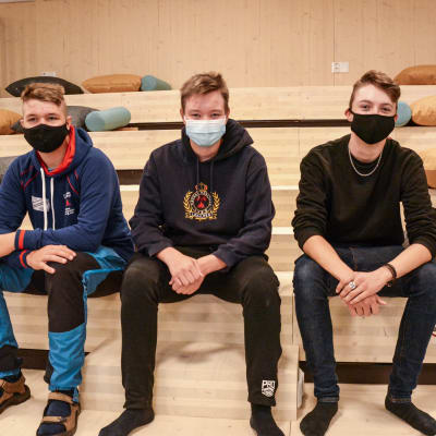 Tre unga män med munskydd sitter på en trätrappa.