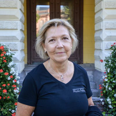 Kvinna står framför ingång med blombuskar bredvid.