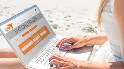 Kvinna använder en dator för att boka flyg på en sandstrand.