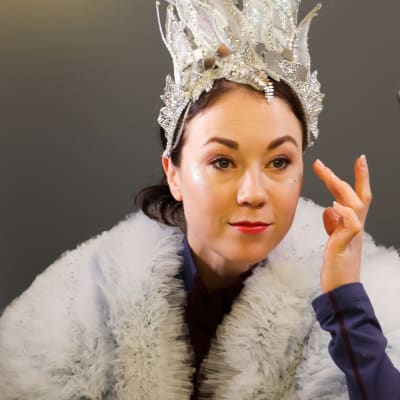 Laura Lepistö gör titelrollen i isshowen Snödrottningen 2022. På bilden sminkar hon sig med vänster hand och tittar genom en spegel.