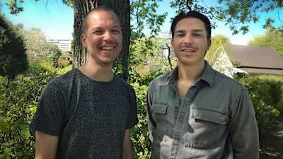 Två män i trettiofemårsåldern, Jonas Welander och Tom Rejström, står framför ett buskage och ett träd och ler mot kameran.
