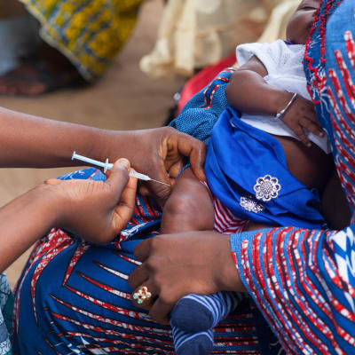 Ett litet barn får en spruta i låret i sin mammas famn.
