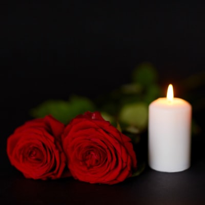 Två röda rosor och ett levande ljus mot en svart bakgrund.