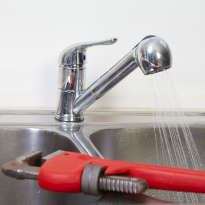En vatten kran med duschmunstycke som det rinner vatten i en ho från. I förgrunden ligger en röd skiftnyckel.