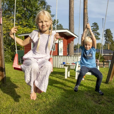 Tyttö ja poika keinuvat kotipihallaan.