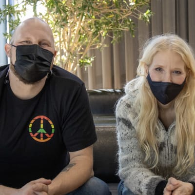 Paleface ja Susan Aho istuvat sohvalla vierekkäin maskit päällä.