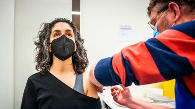 En kvinna i munskydd får en dos coronavaccin i armen.