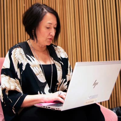 En kvinna sitter i en fotölj men en bärbar dator i famnen.