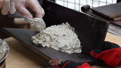 En hand med engångshandske håller i en sked och formar en igloo-formad form av betong på en vinkel av vattenfast faner för att använda till en svalholk av träbetong.