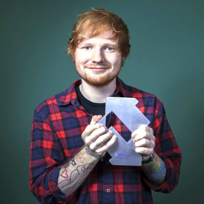 Ed Sheeran håller i en pokal och ler.