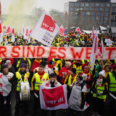 Keltaliivisiä mielenosoittajia ja kyltti, jossa lukee "15%, OLEMME SEN ARVOISIA" saksaksi.