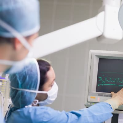 Läkare i skyddsutrustning kollar på en skärm där man ser ett hjärtslag.