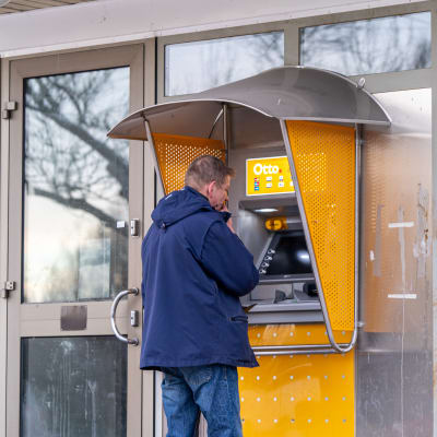 Medelålders man i blå jacka står framför en bankomat. 
