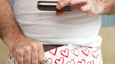 En bild av en man som fotar ner i sina boxershorts, med en mobiltelefon.