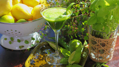 Grön dryck i cocktailglas dekorerad med två basilika blad.