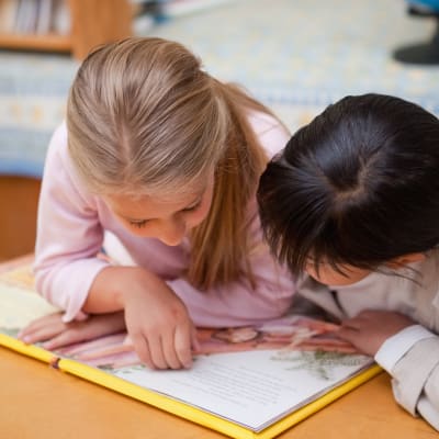 Två flickor läser en bok. 