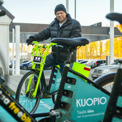 Kuopion kaupungin liikkumispalveluiden kehittämispäällikkö Jouni Huhtinen kaupunkipyörän selässä Kuopion-hallin edustalla.