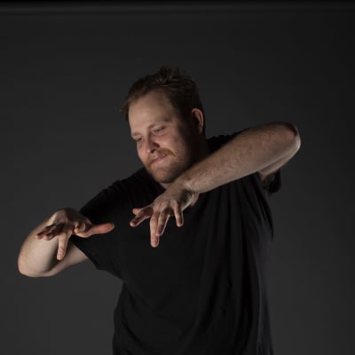 Jonas spelar luftpiano med armarna i en mörklagd studio.