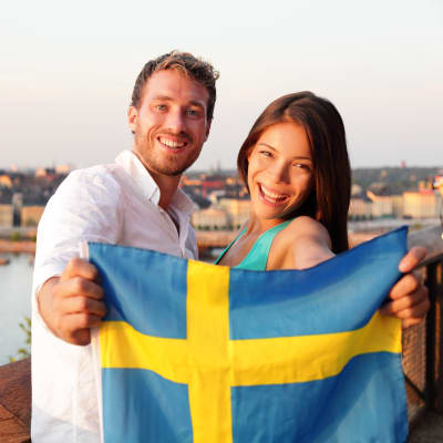 En man och en kvinna håller i en svensk flagga i förgrunden av Stockholm.