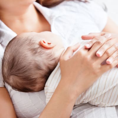 ett spädbarn som vilar på mammans bröstkorg. Mamman håller sina händer om den lilla barnkroppen