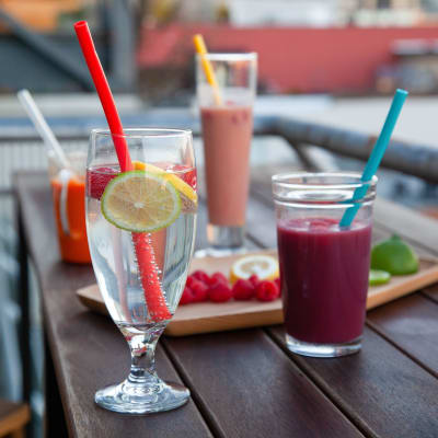 Glas med sugrör i står på ett bord. Glasen har olika saker i, t.ex. smoothie och vatten. På bordet finns också en bricka med frukt.