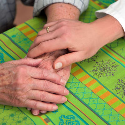 Yngre hand på två rynkiga, äldre händer på bordet.
