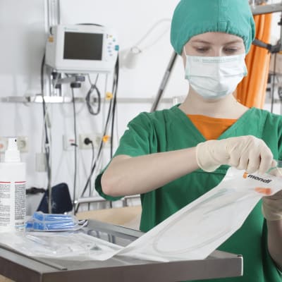 Skötare med ansiktsmask öppnar engångsförpackning med vårdartikel.