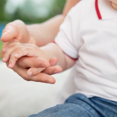 Ett litet barn håller sin förälder i handen.