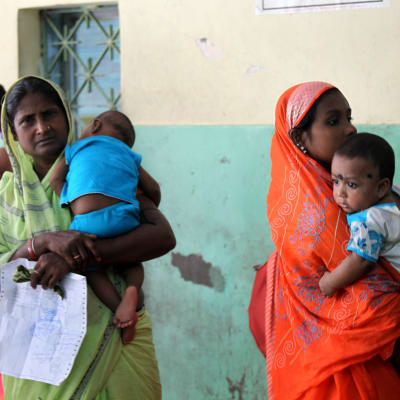 Mammor köar för vård för sina barn på ett sjukhus i Calcutta