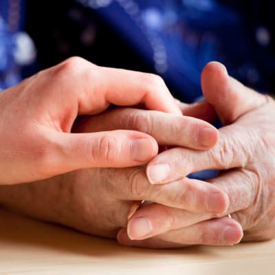 händer. en äldre persons knäppta händer och så en yngre människas hand ovanpå
