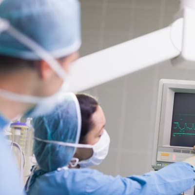 Läkare i skyddsutrustning kollar på en skärm där man ser ett hjärtslag.