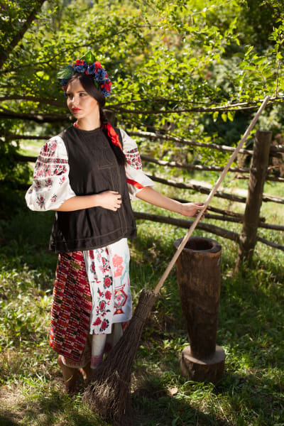 En ukrainsk kvinna i traditionella sommarkläder och en kvast i handen.