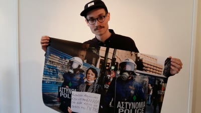 Erik Åhman håller upp en av sina bilder från Grekland. Bilden visar en demonstrerande kvinna omgiven av poliser.