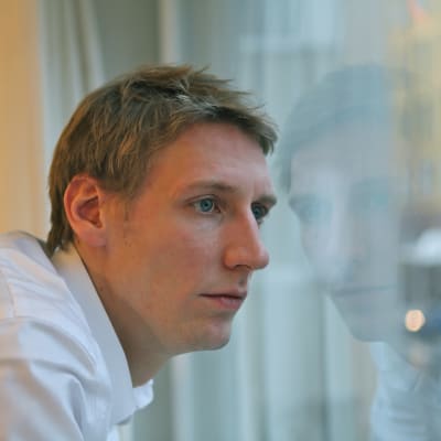 Pekka Strang i profil tittar ut genom ett fönster.