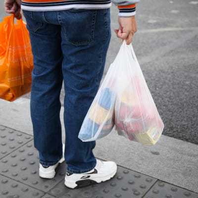 En man som håller i tre plastpåsar fyllda med matvaror.
