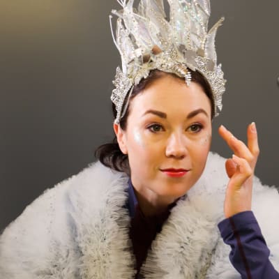 Laura Lepistö gör titelrollen i isshowen Snödrottningen 2022. På bilden sminkar hon sig med vänster hand och tittar genom en spegel.