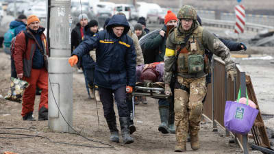 Soldater och räddningsarbetare bär på en person som ligger på en brits.