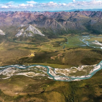 Alaskan arktisen luonnonsuojelualueen maisemaa kirkkaan sininen joki ja taustalla vuorenhuippuja