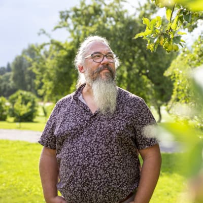 Ekologiprofessor Janne Kotiaho, i kortärmad skjorta bland träd på en gräsmatta.