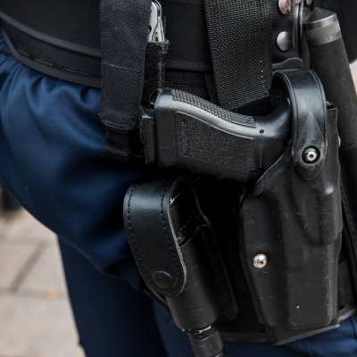 En polis som bär på ett skjutvapen. Bilden är en närbild av skjutvapnet som är fast i ett bälte.