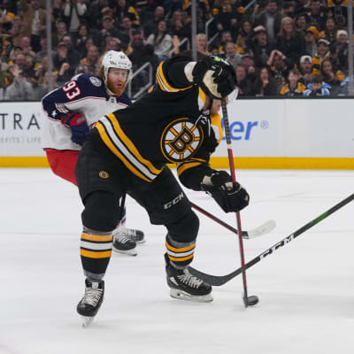 Svartklädd spelare skjuter pucken mot mål i match mot vitklätt lag.