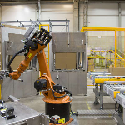 En orange robot som monterar ihop paket i postens logistikcentral för näthandel i Vanda.