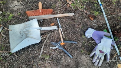 Olika arkeologiska verktyg på marken: En borste, en tandborste, en sekatör, en sopskyffel och ett par handskar.