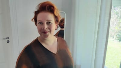Kvinna med rött hår och brun klänning.